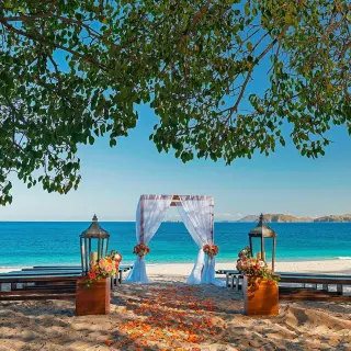 Beachfront wedding ceremony with a white fabric arch and wooden benches at Westin Reserva Conchal, Liberia