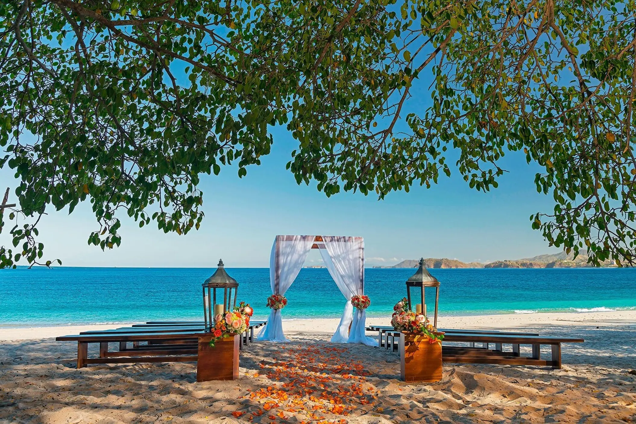 Beachfront wedding ceremony with a white fabric arch and wooden benches at Westin Reserva Conchal, Liberia