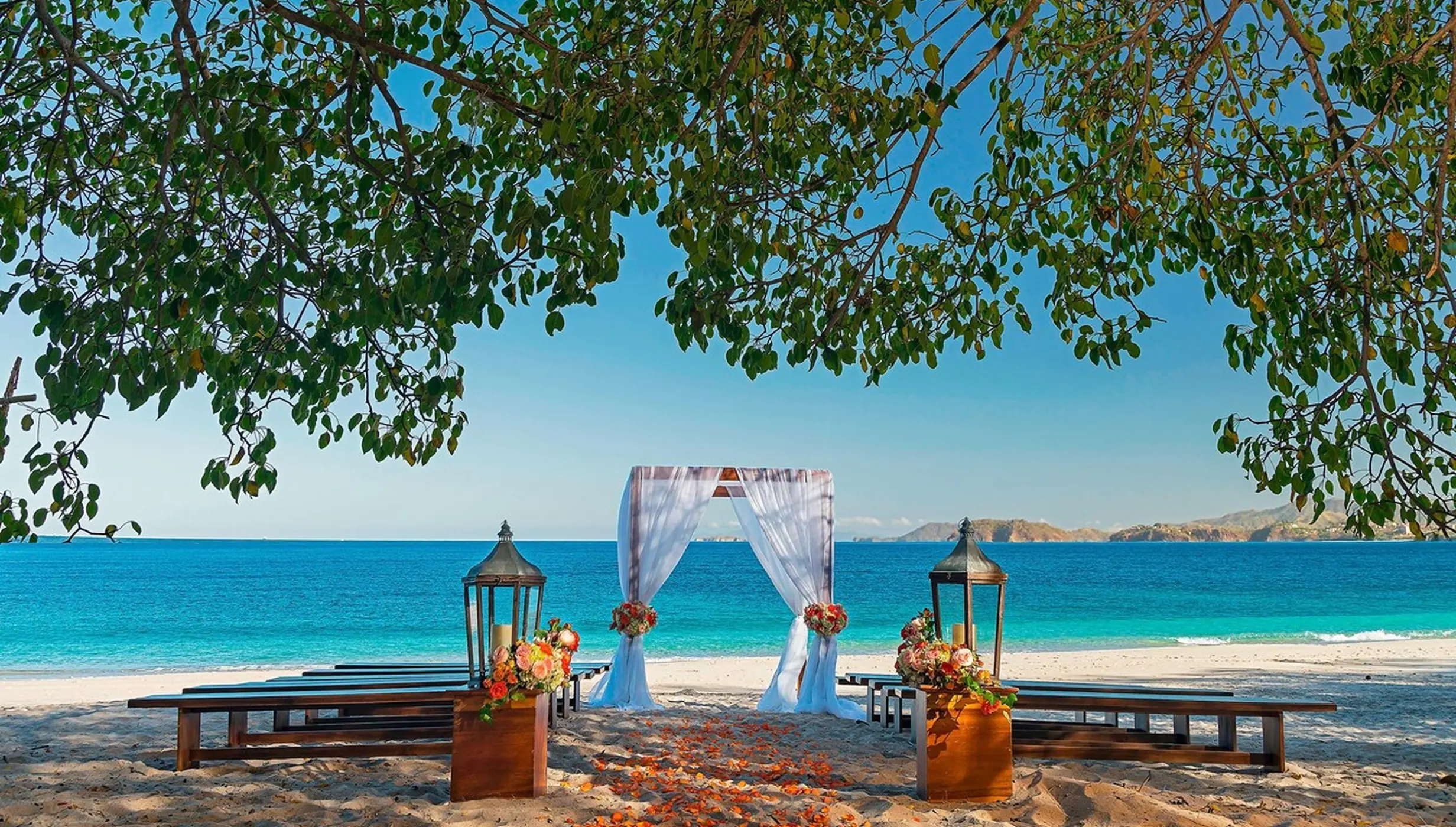 Beachfront wedding ceremony with a white fabric arch and wooden benches at Westin Reserva Conchal, Liberia