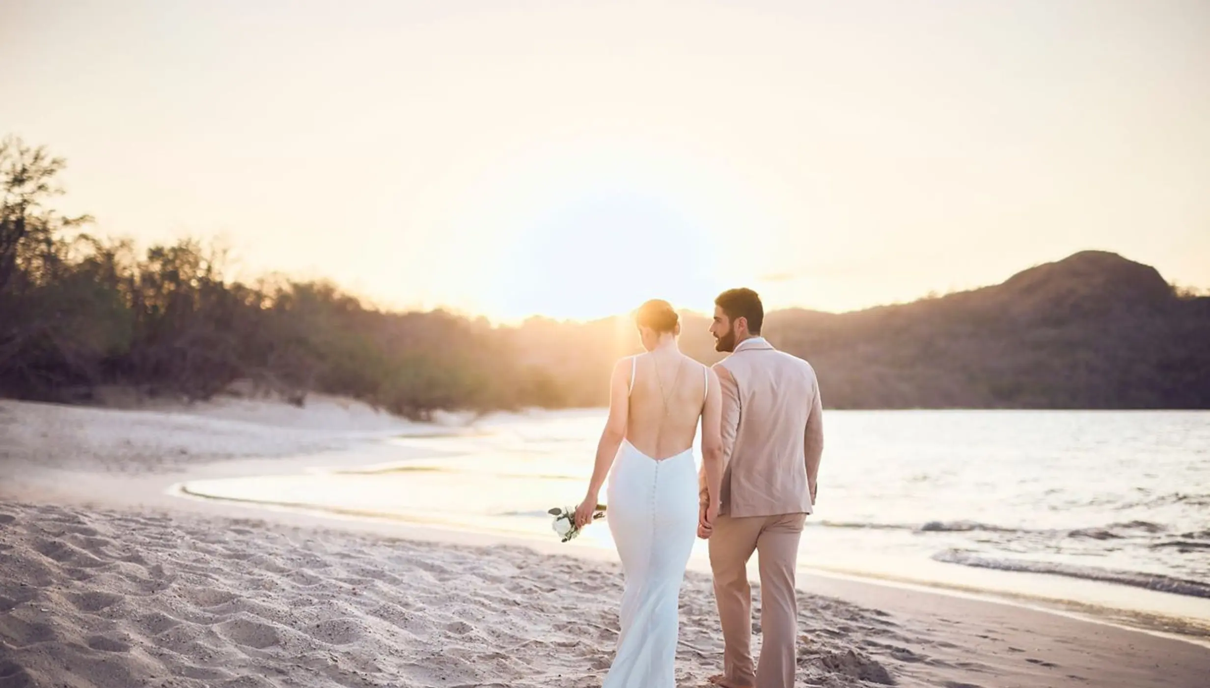 Bride and groom walking at sunset on the beach at The Westin Reserva Conchal, Liberia