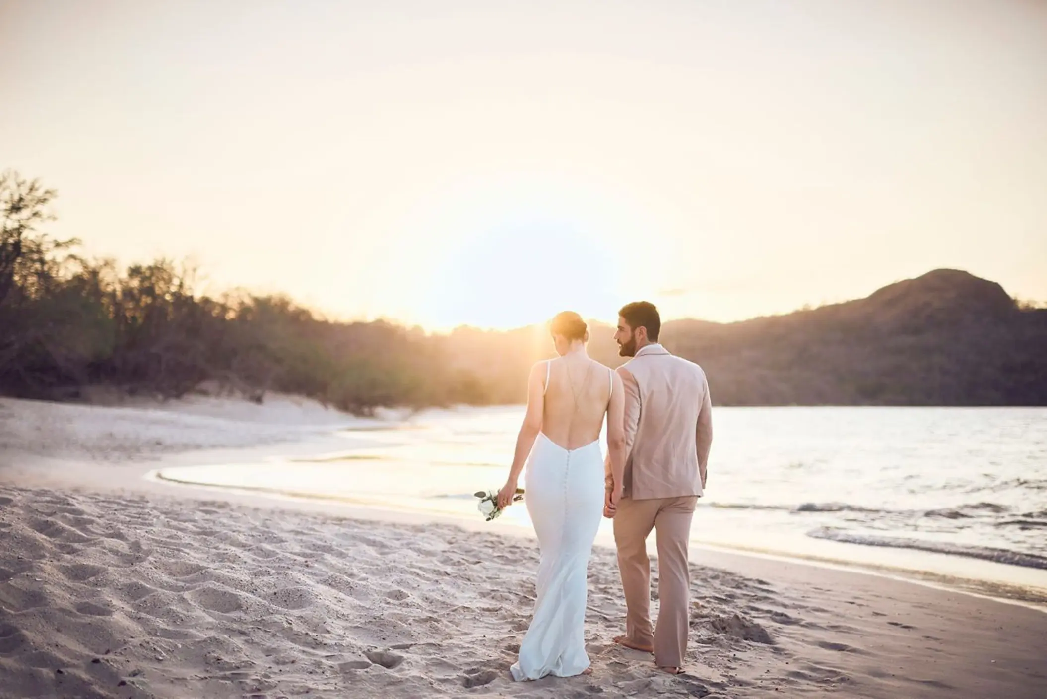 Bride and groom walking at sunset on the beach at The Westin Reserva Conchal, Liberia