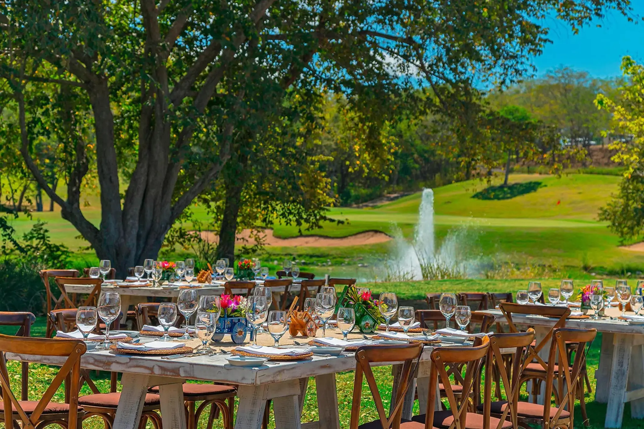 Outdoor wedding reception setup with wooden tables by a fountain and golf course at Westin Reserva Conchal, Liberia