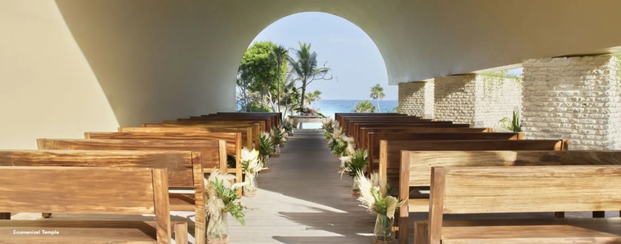 Ecumenical chapel wedding ceremony setup with wooden pews at Hotel Xcaret Arte, Riviera Maya