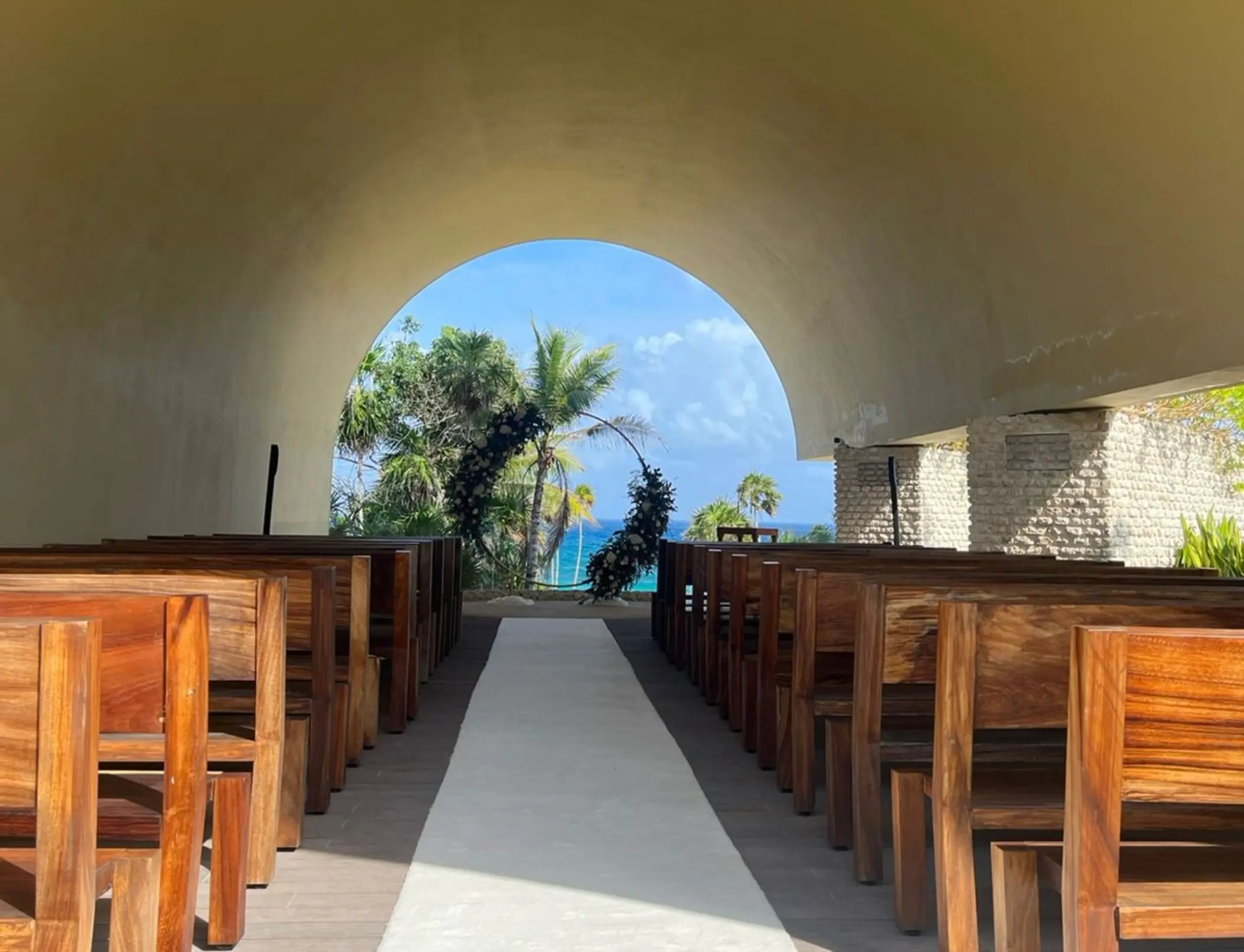 Ecumenical chapel wedding ceremony setup with wooden pews at Hotel Xcaret Arte, Riviera Maya
