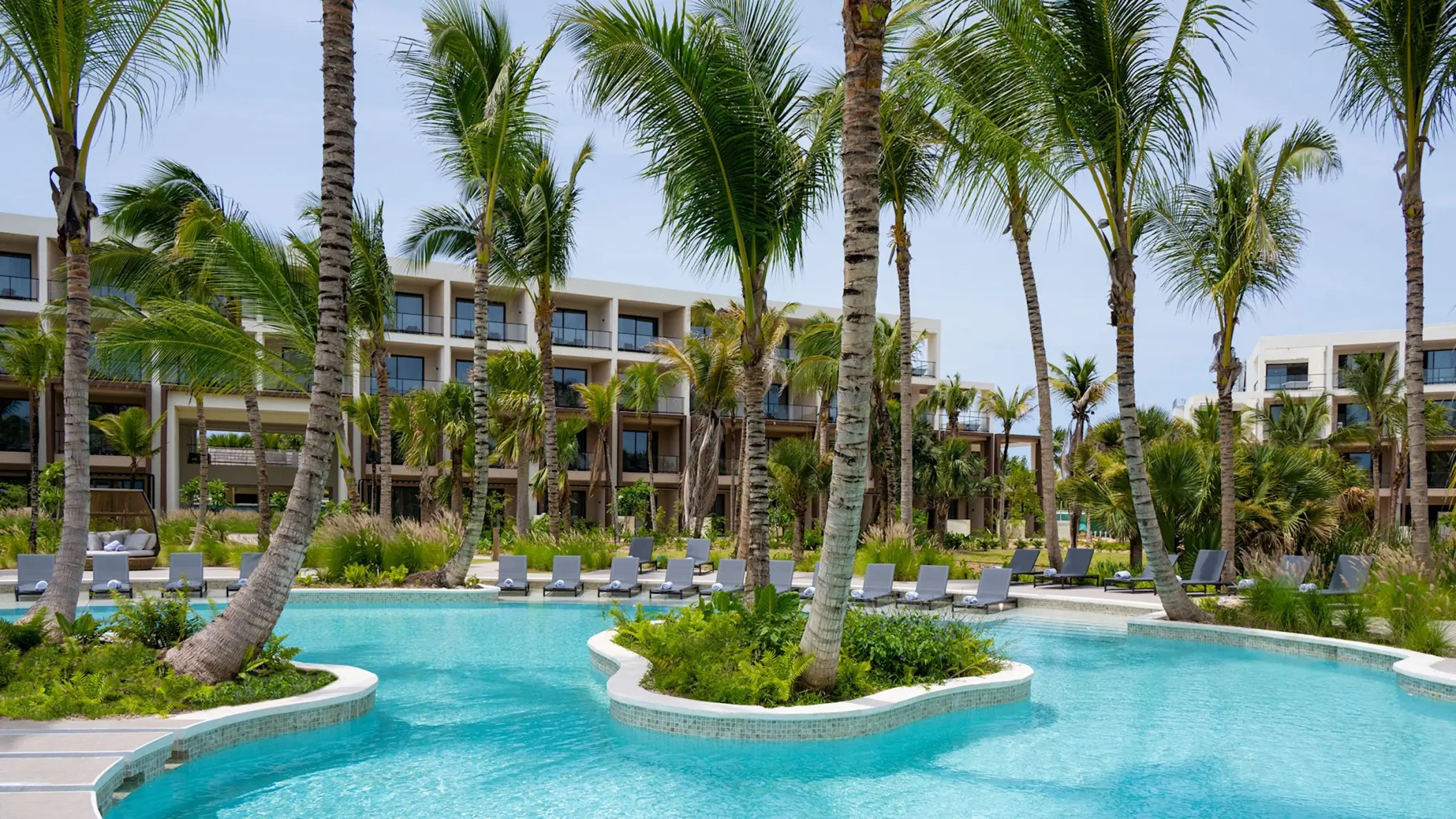 Curving outdoor swimming pool with lounge chairs and palm trees at Zemi Miches, Punta Cana