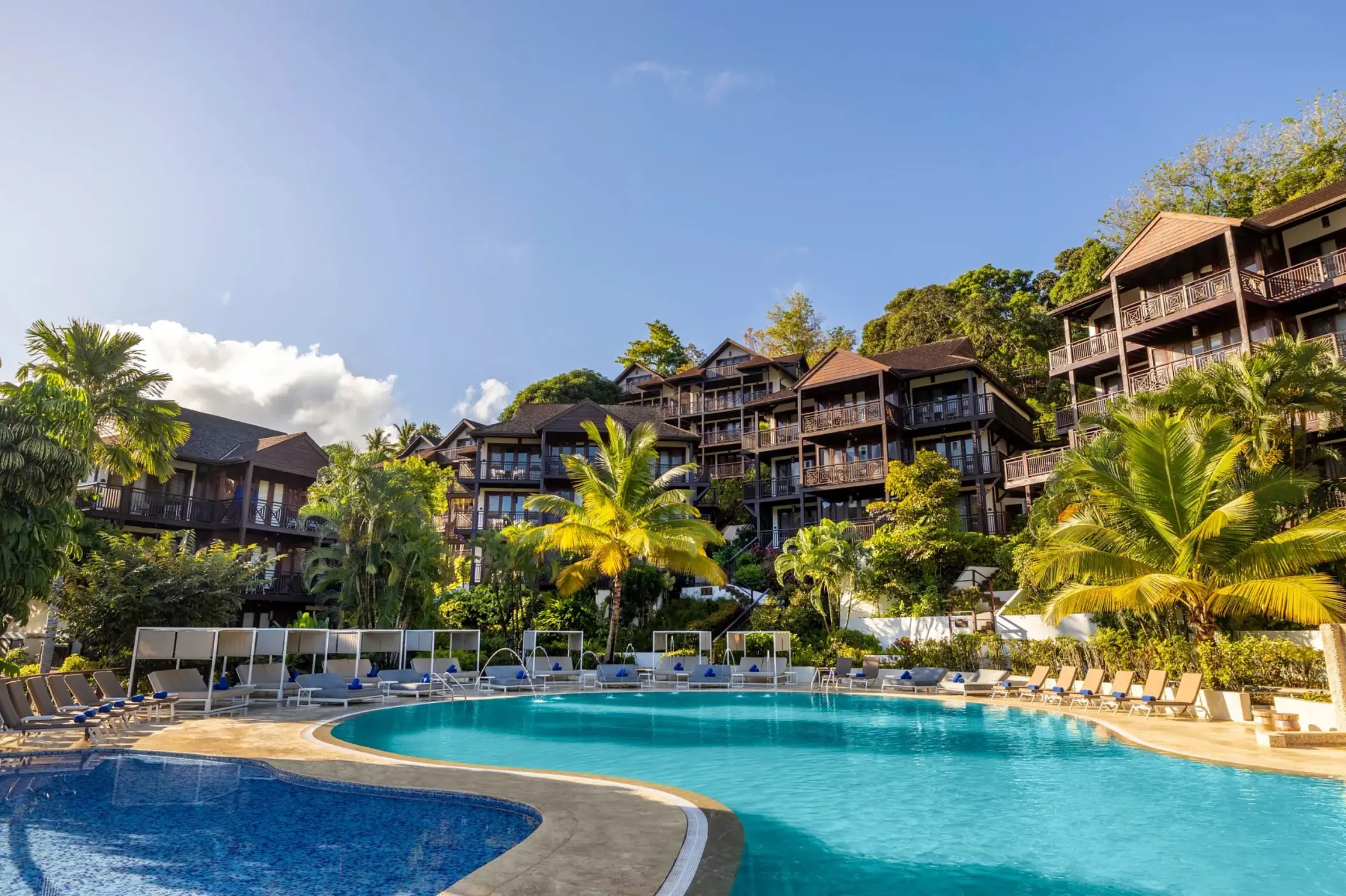 Main swimming pool surrounded by palm trees and hillside suites at Zoetry Marigot Bay, Castries