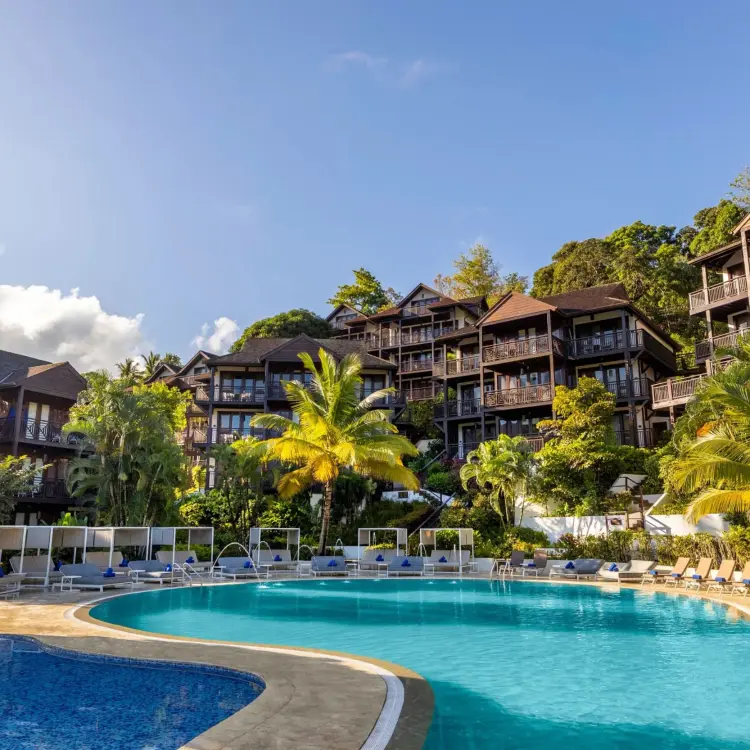 Main swimming pool surrounded by palm trees and hillside suites at Zoetry Marigot Bay, Castries