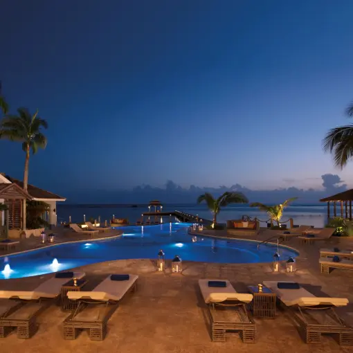 Main pool with blue lighting and lounge chairs at dusk at Zoetry Montego Bay