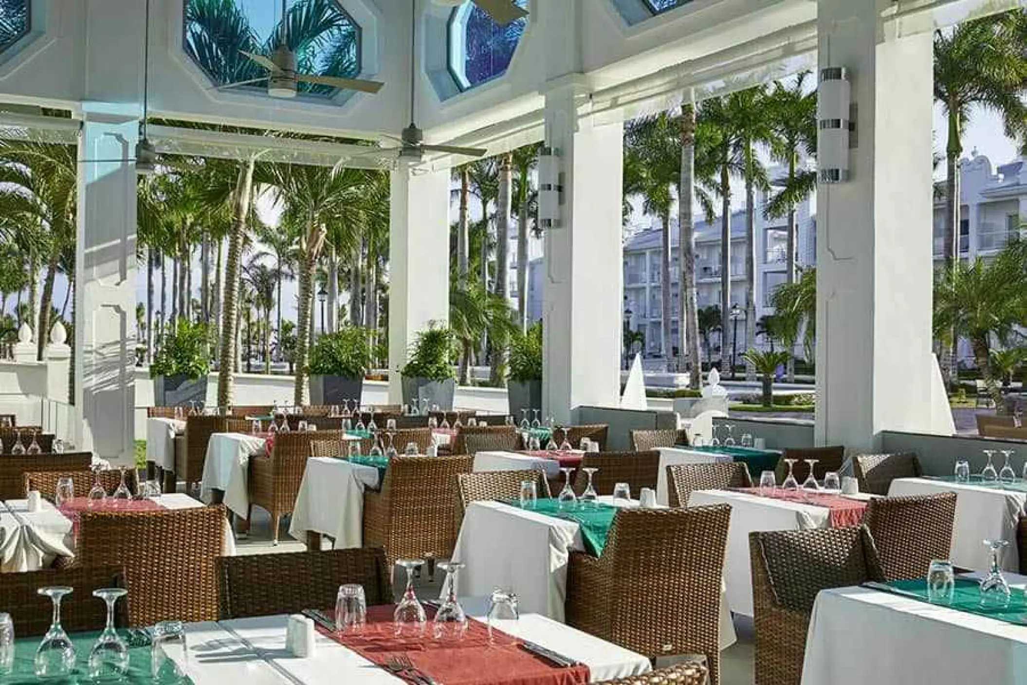 Outdoor restaurant terrace with set tables and palm tree views at Riu Palace Riviera Maya, Playa Del Carmen