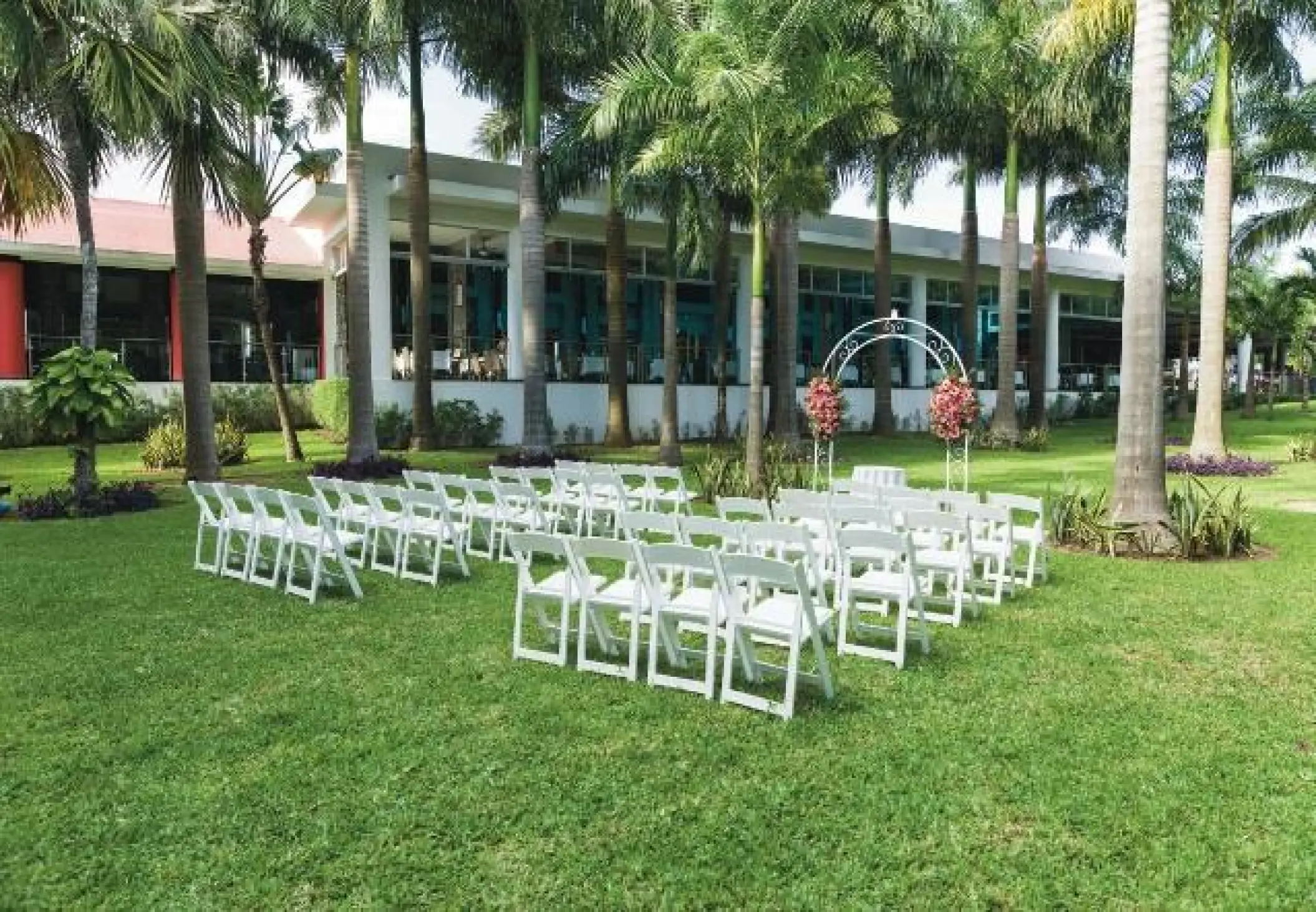 Garden wedding ceremony setup with white chairs and floral arch at Riu Yucatan, Playa Del Carmen