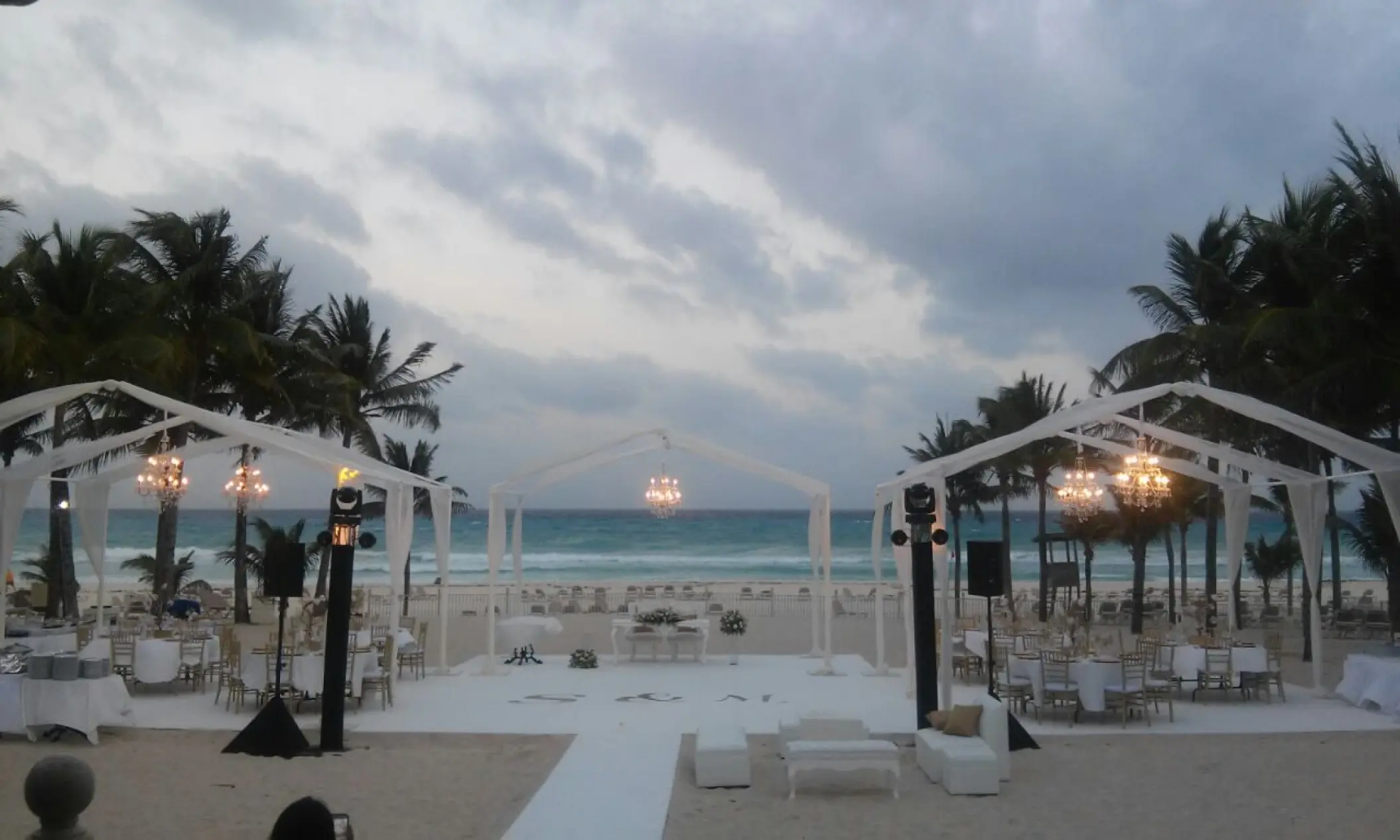 Outdoor beach wedding reception with white tents and chandeliers at Riu Palace Costa Mujeres, Cancun
