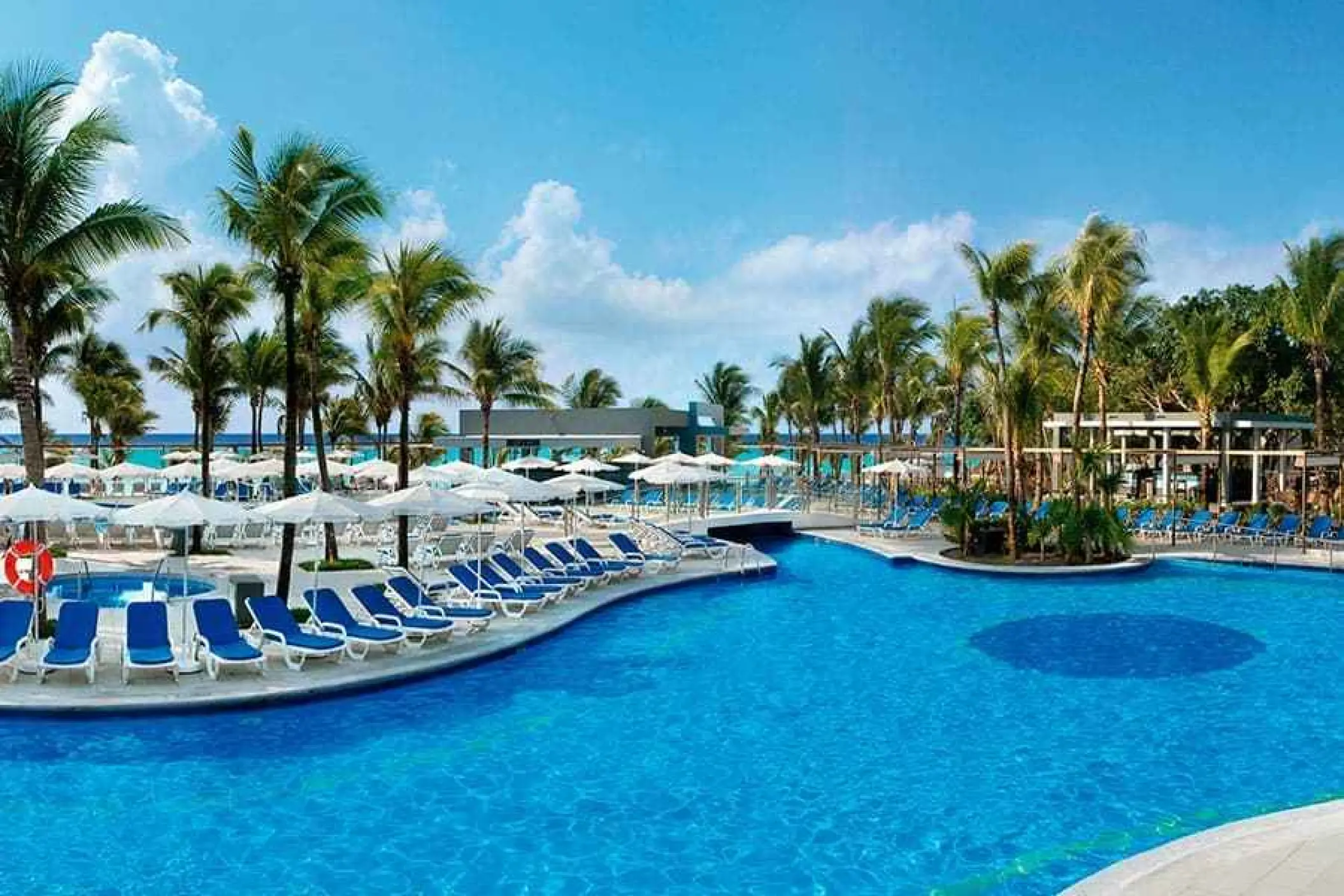 Outdoor swimming pool with blue lounge chairs and white umbrellas at Riu Yucatan, Playa Del Carmen
