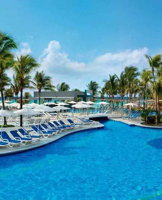 Outdoor swimming pool with blue lounge chairs and white umbrellas at Riu Yucatan, Playa Del Carmen