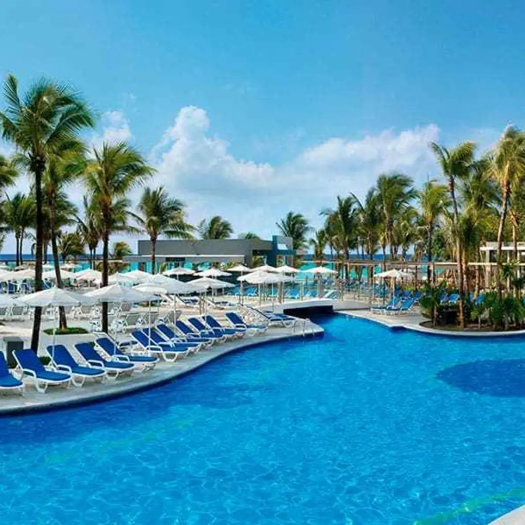 Outdoor swimming pool with blue lounge chairs and white umbrellas at Riu Yucatan, Playa Del Carmen
