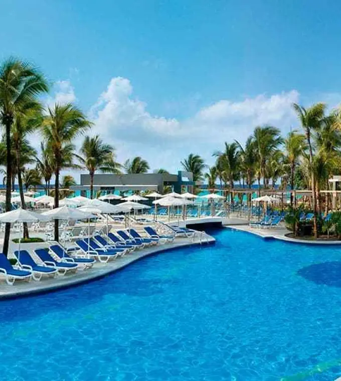 Outdoor swimming pool with blue lounge chairs and white umbrellas at Riu Yucatan, Playa Del Carmen