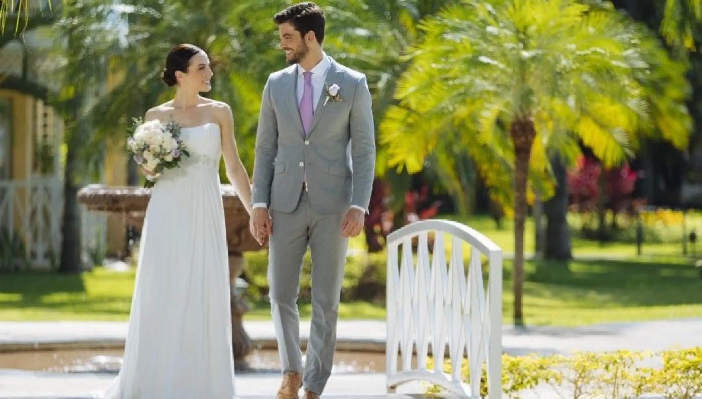 Bride and groom walking across a white garden bridge at Royal Hideaway Playacar, Playa Del Carmen