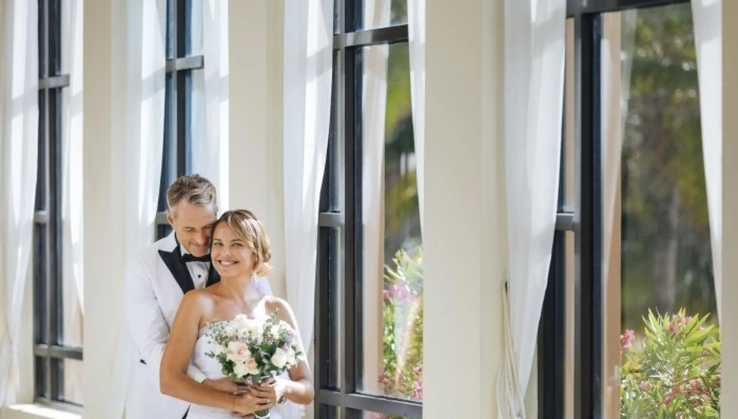 Bride and groom posing by tall windows with white drapes at Royal Hideaway Playacar, Playa Del Carmen
