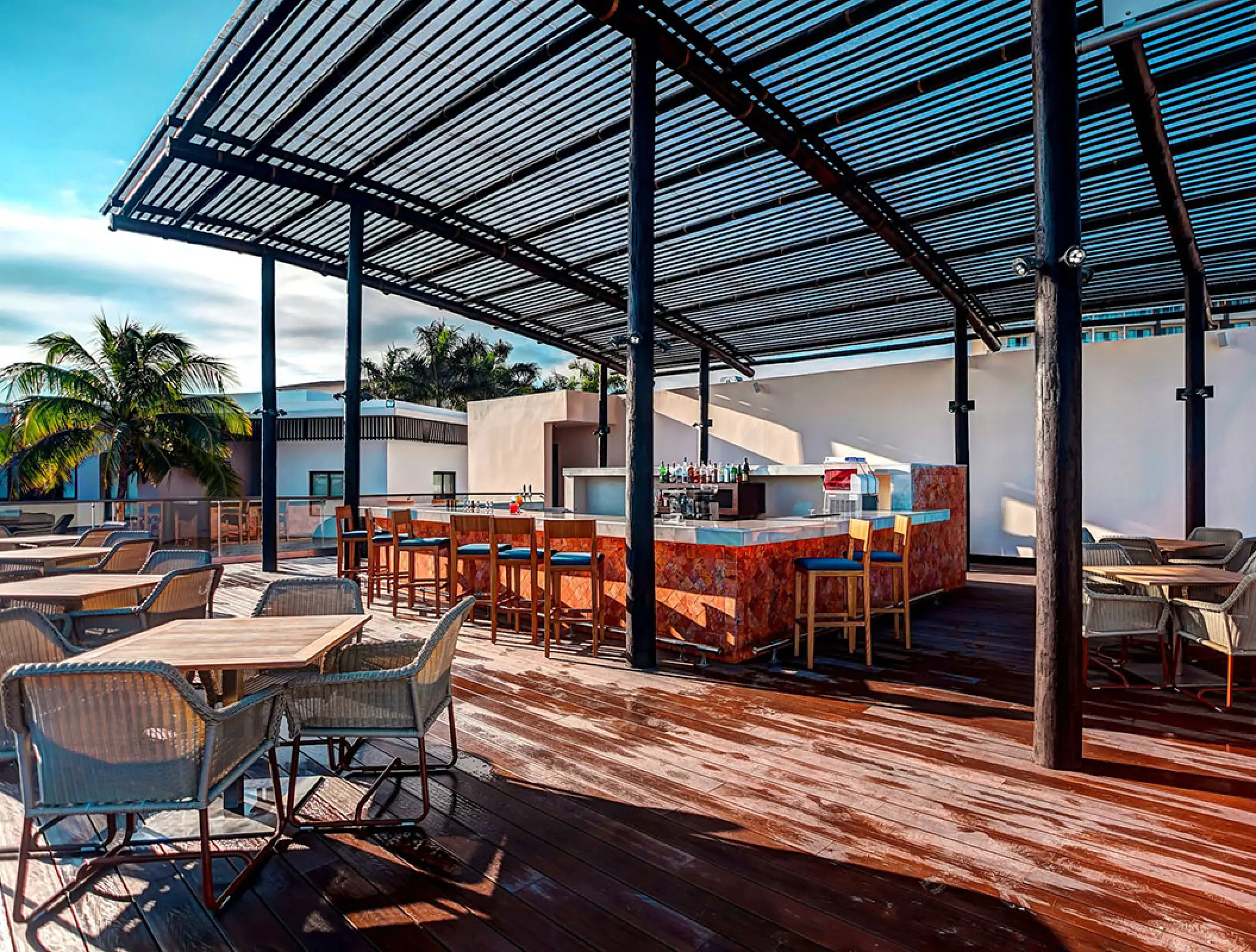 Outdoor rooftop bar and wooden dining tables under a pergola at Royalton Blue Waters, Montego Bay