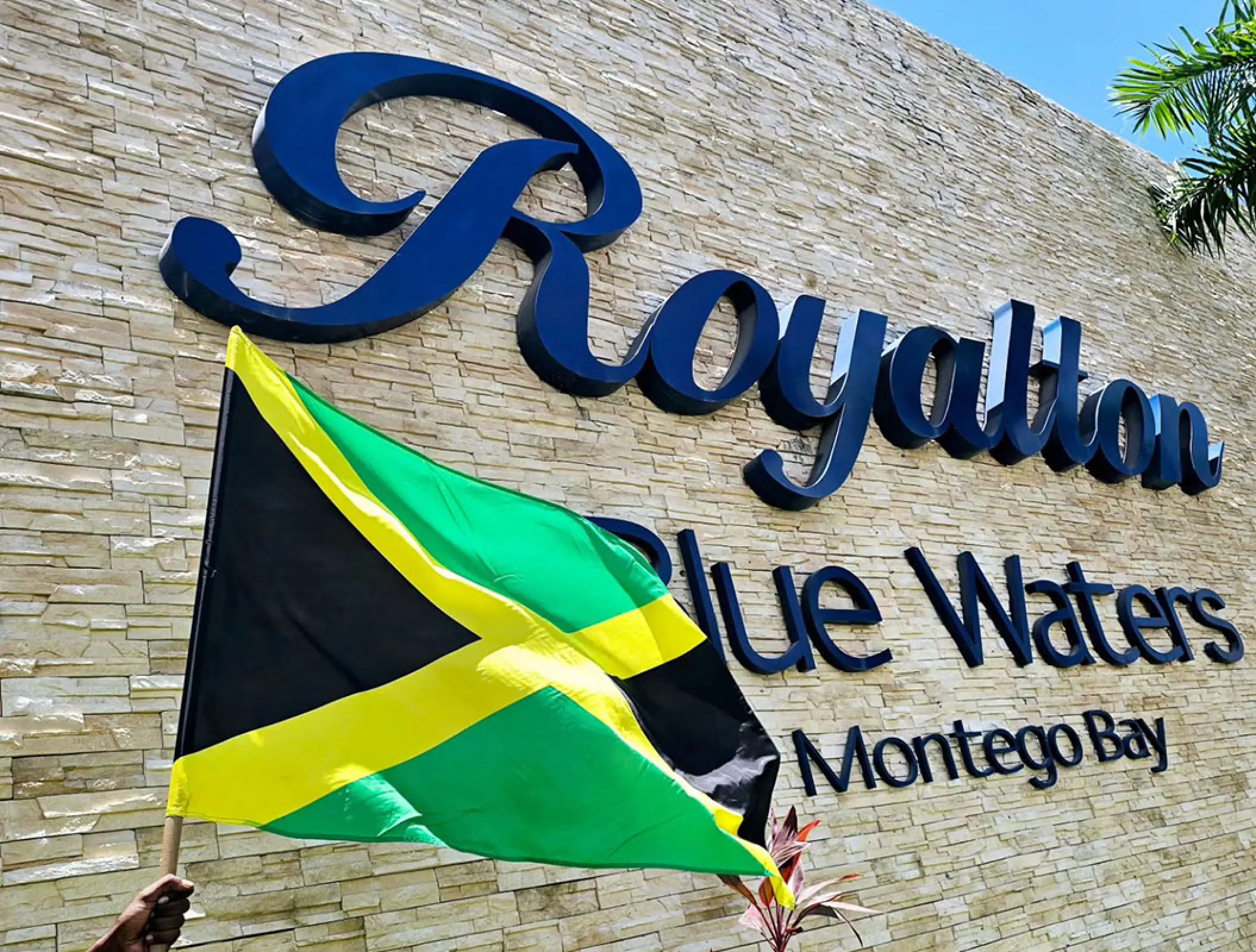 Jamaica flag held in front of the Royalton Blue Waters sign, Montego Bay