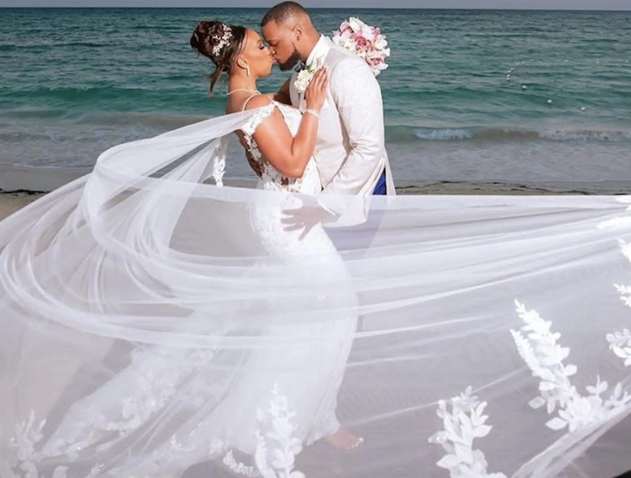 Bride and groom kissing on the beach with a long flowing veil at Royalton Blue Waters, Montego Bay