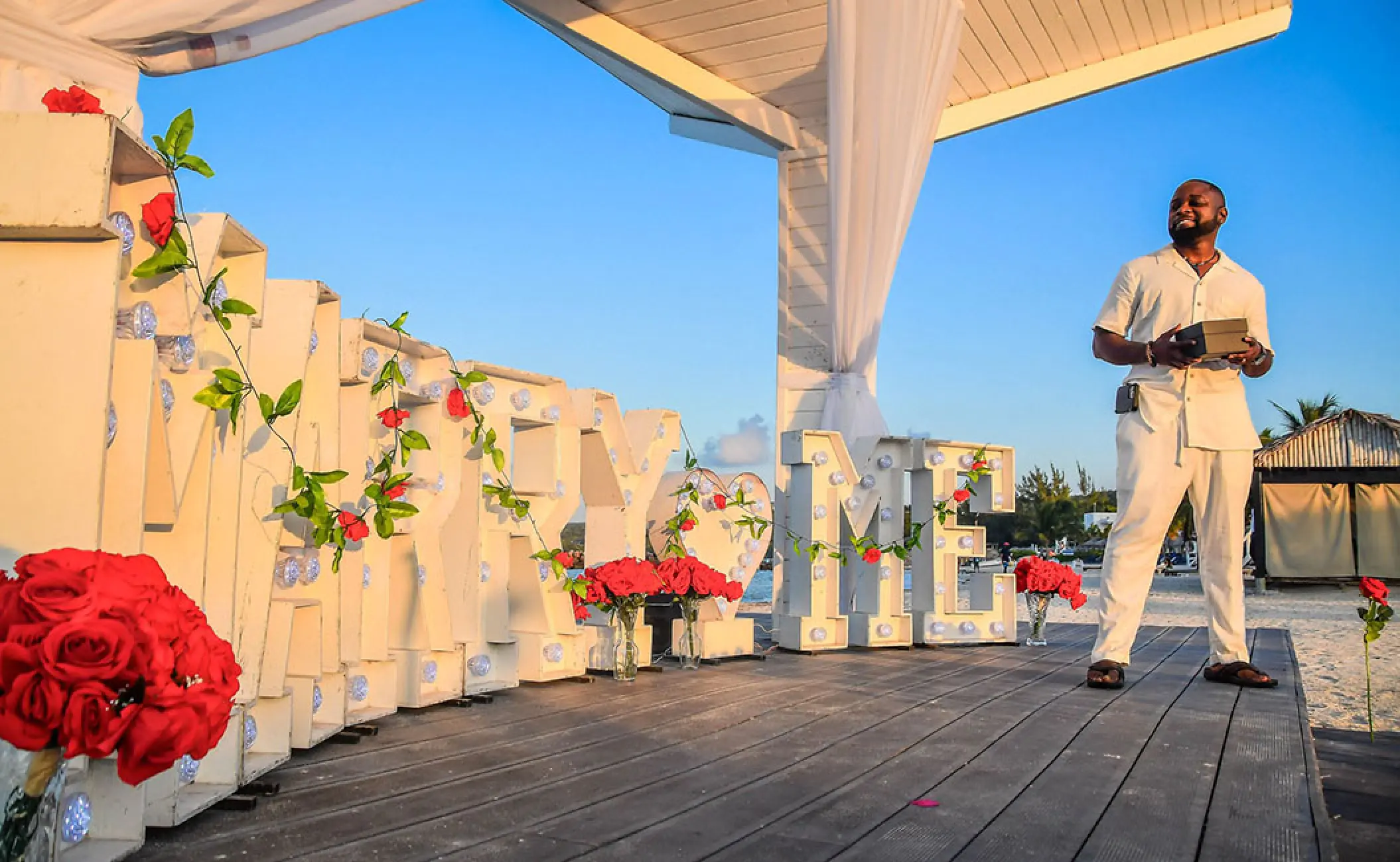 Groom standing by Marry Me light-up letters for a beach proposal at Royalton Blue Waters, Montego Bay