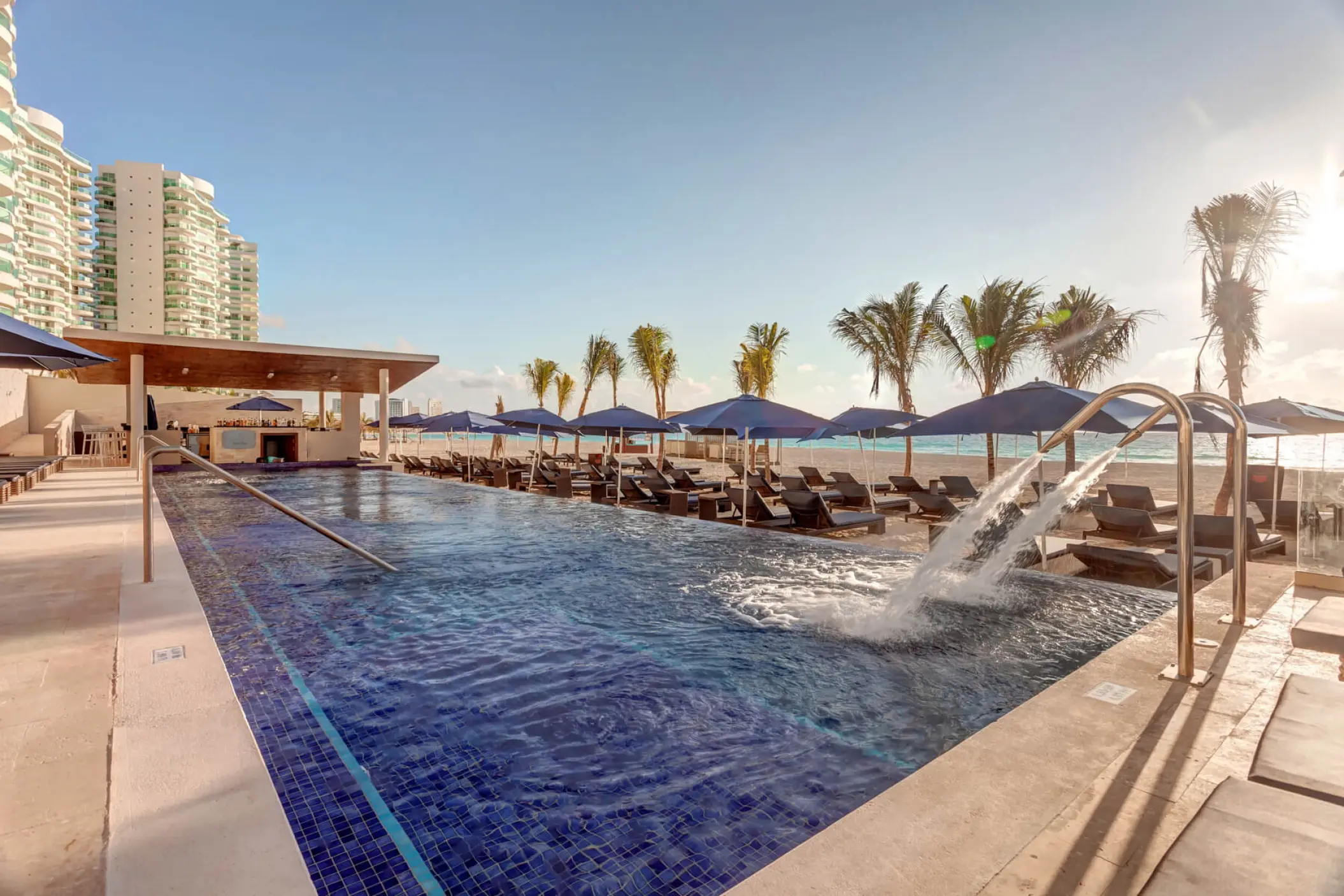 Royalton CHIC Cancun main pool with water fountains and blue umbrellas, Cancun