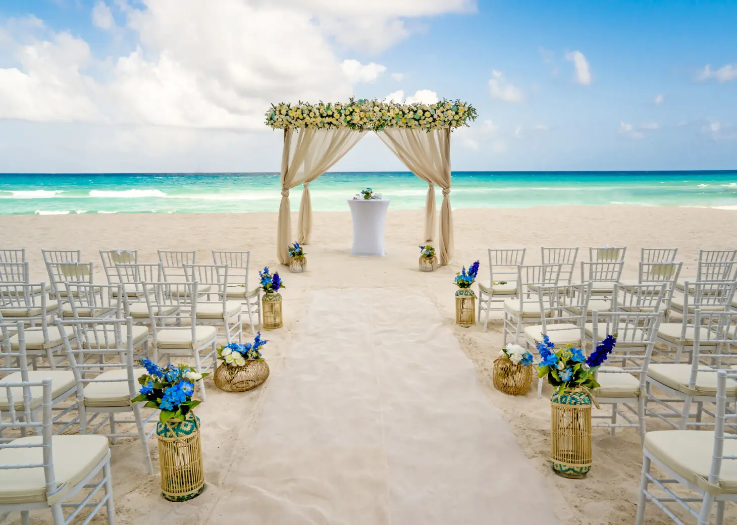 Beachfront wedding ceremony with a floral arch and white chairs at Royalton CHIC Cancun, Cancun