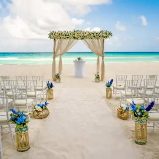 Beachfront wedding ceremony with a floral arch and white chairs at Royalton CHIC Cancun, Cancun
