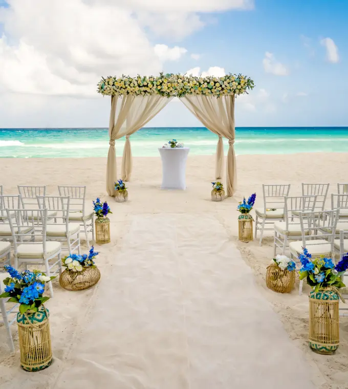 Beachfront wedding ceremony with a floral arch and white chairs at Royalton CHIC Cancun, Cancun
