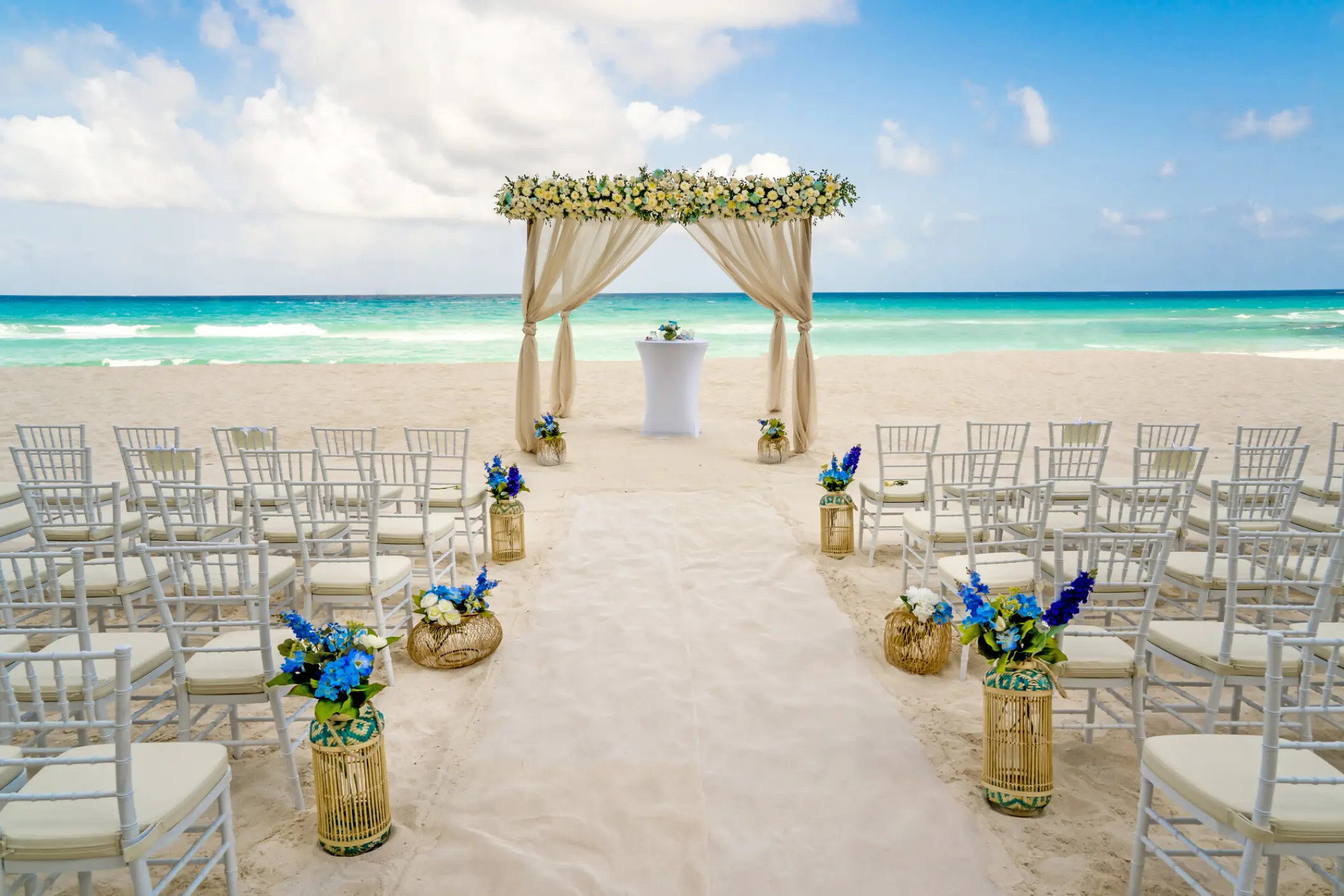 Beachfront wedding ceremony with a floral arch and white chairs at Royalton CHIC Cancun, Cancun