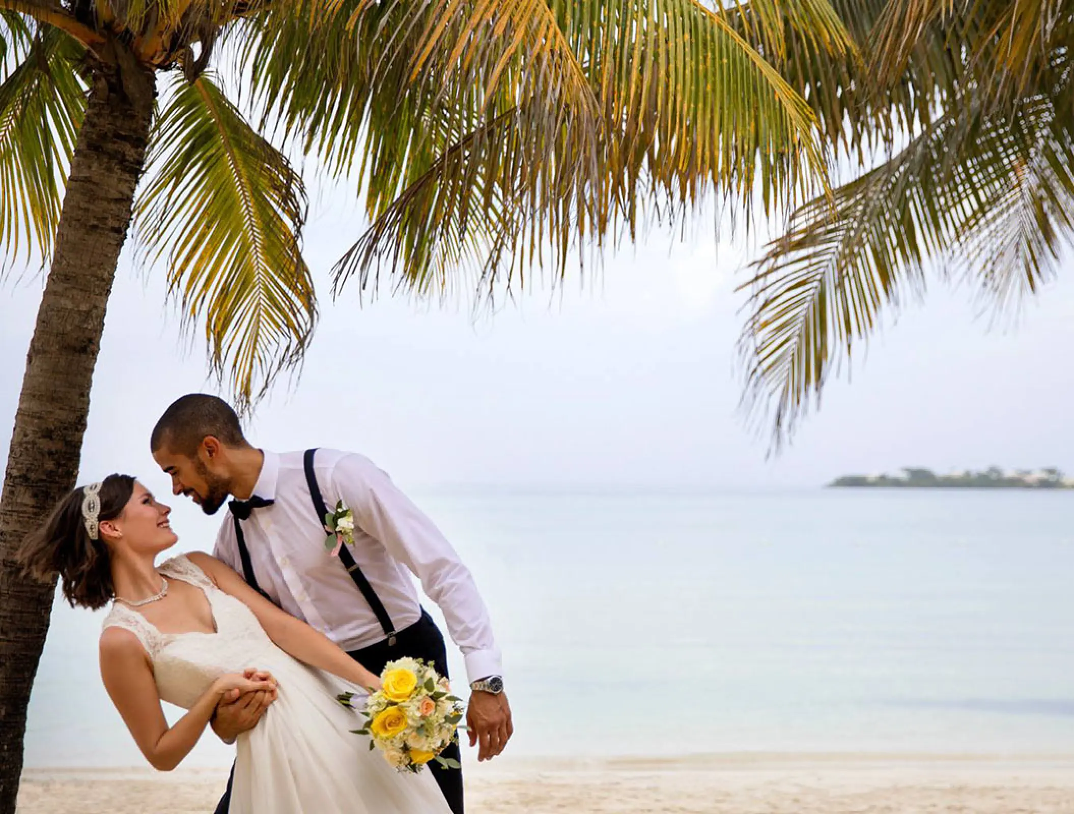 Groom dipping the bride during a beach portrait under palm fronds at Royalton Negril, Negril