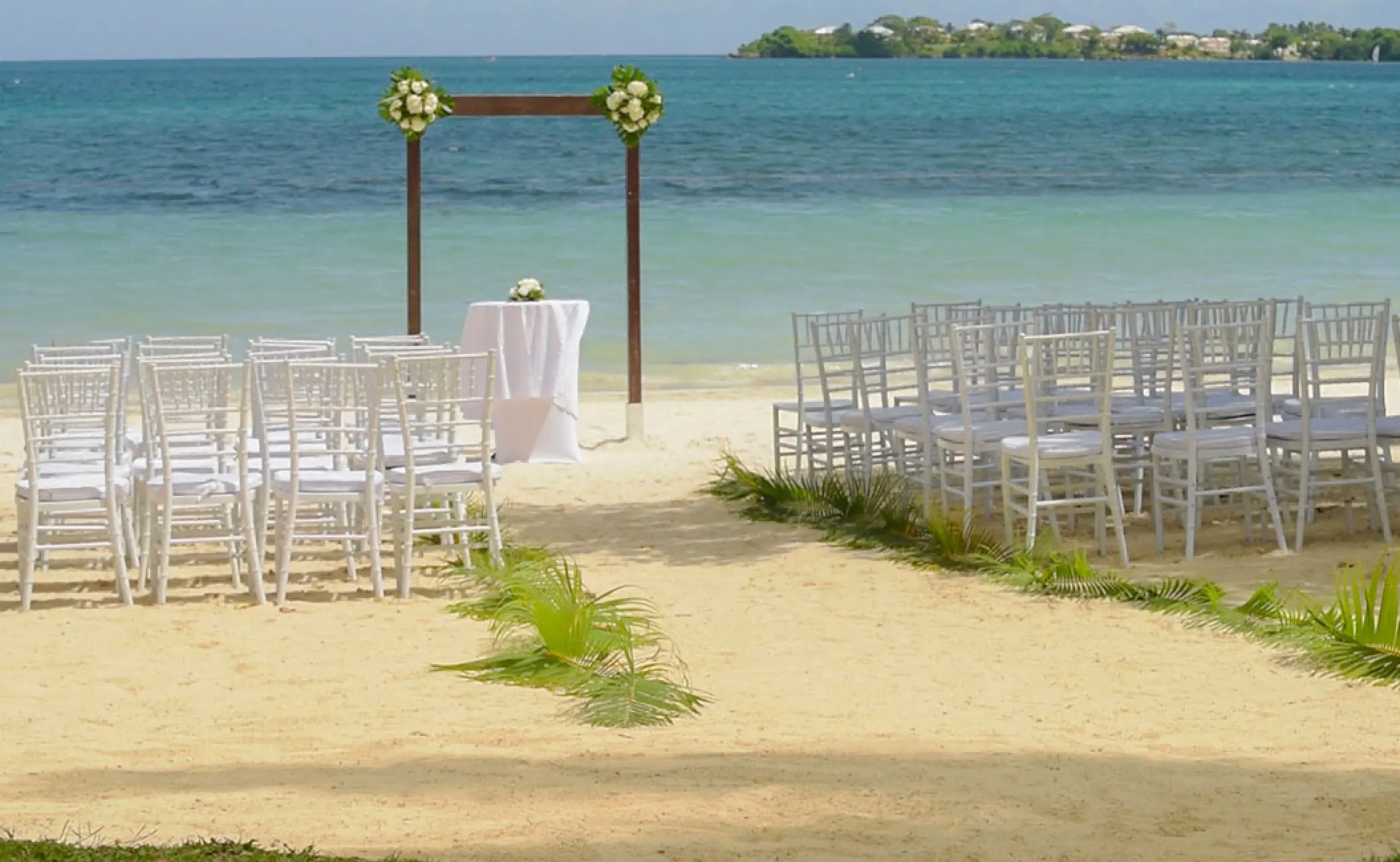 Beachfront wedding ceremony with white chairs and floral arch at Royalton Negril, Negril