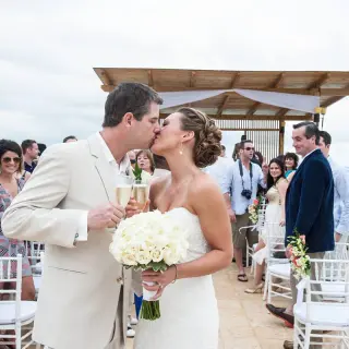 The couple kissing and holding champagne glasses after their wedding ceremony at Royalton Blue Waters, Montego Bay