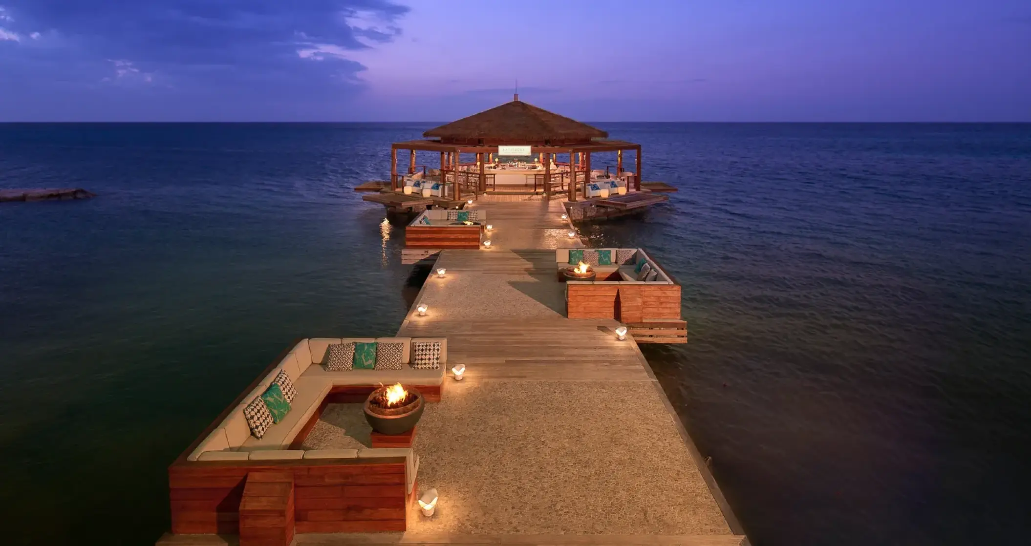 Over-the-water bar and lounge with fire pits at Sandals Montego Bay at dusk