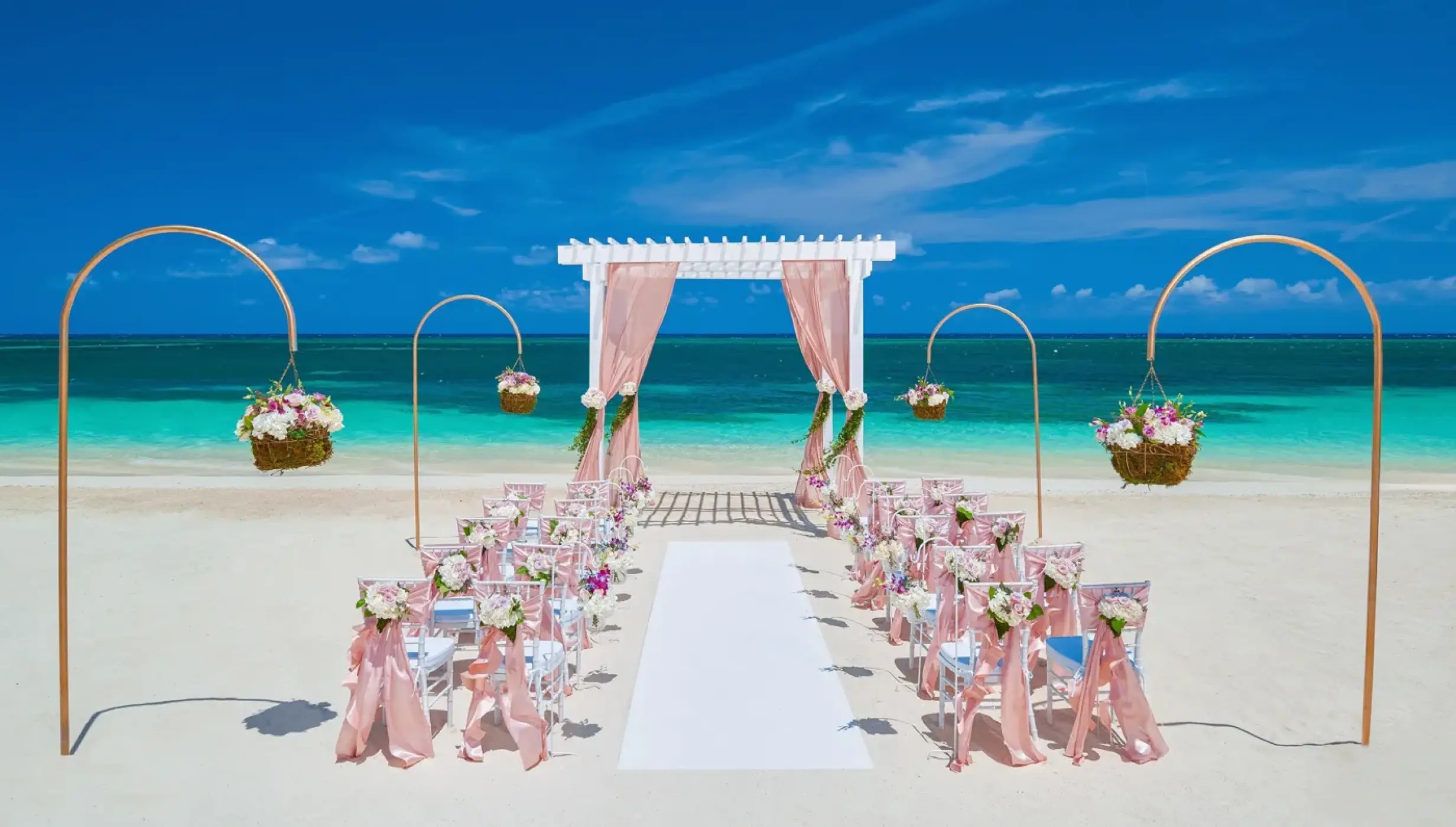 Beachfront wedding ceremony with a pink draped gazebo and floral decor at Sandals Montego Bay
