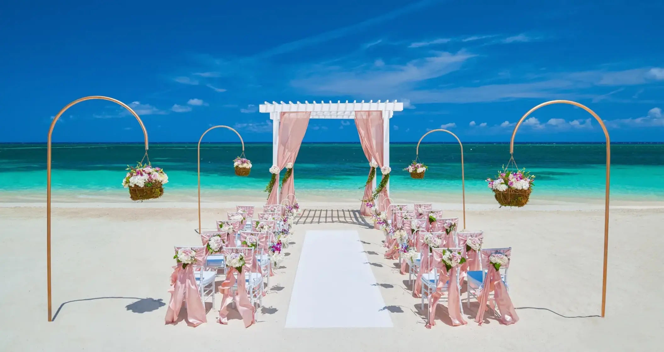 Beachfront wedding ceremony with a pink draped gazebo and floral decor at Sandals Montego Bay
