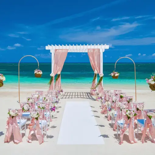 Beachfront wedding ceremony with a pink draped gazebo and floral decor at Sandals Montego Bay