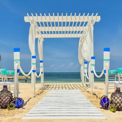 Beachfront wedding ceremony setup with a white pergola and teal chairs at Sandals Montego Bay
