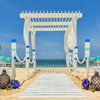 Beachfront wedding ceremony setup with a white pergola and teal chairs at Sandals Montego Bay