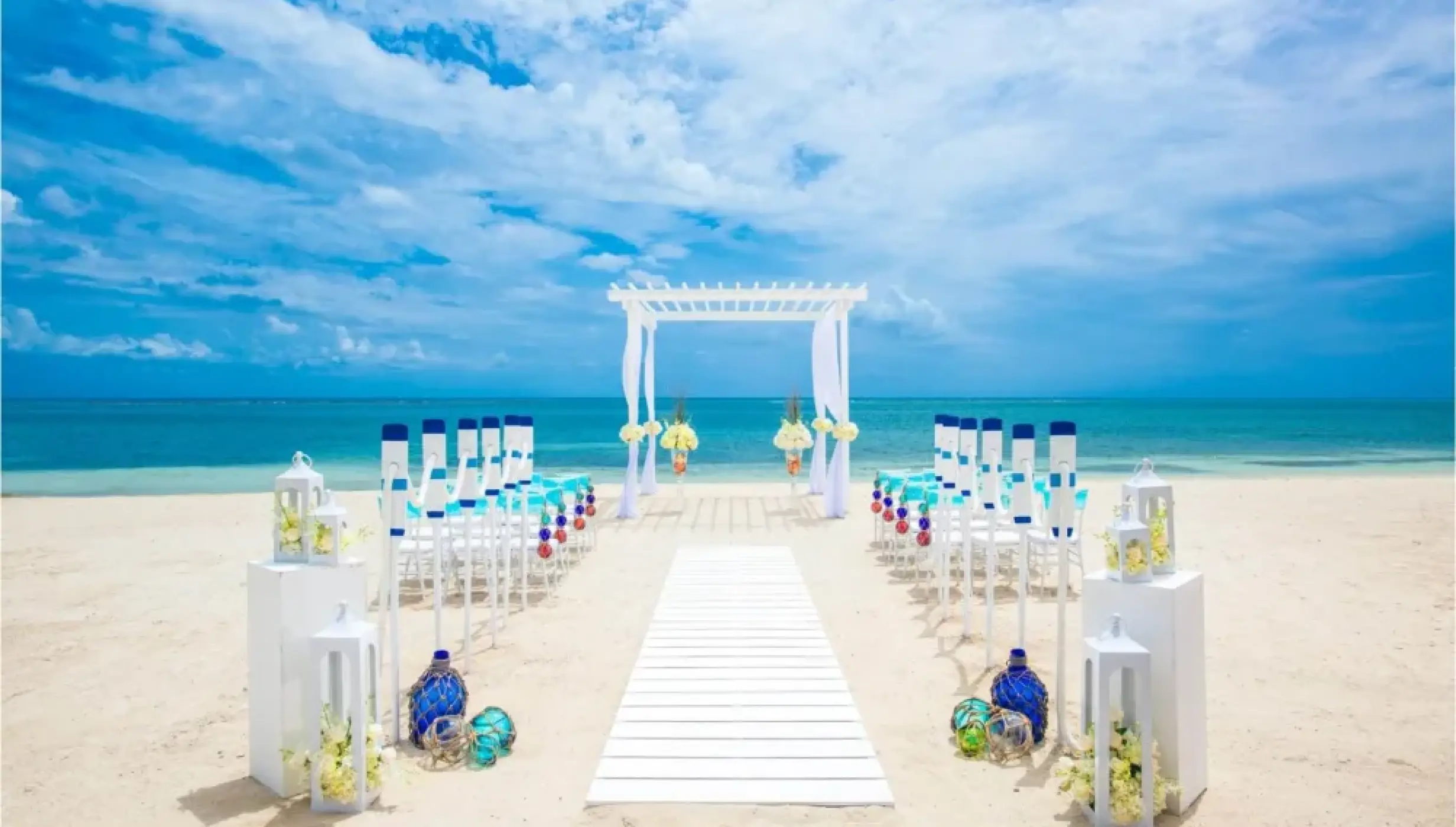 Beachfront wedding ceremony with white pergola and blue accents at Sandals Montego Bay, Montego Bay