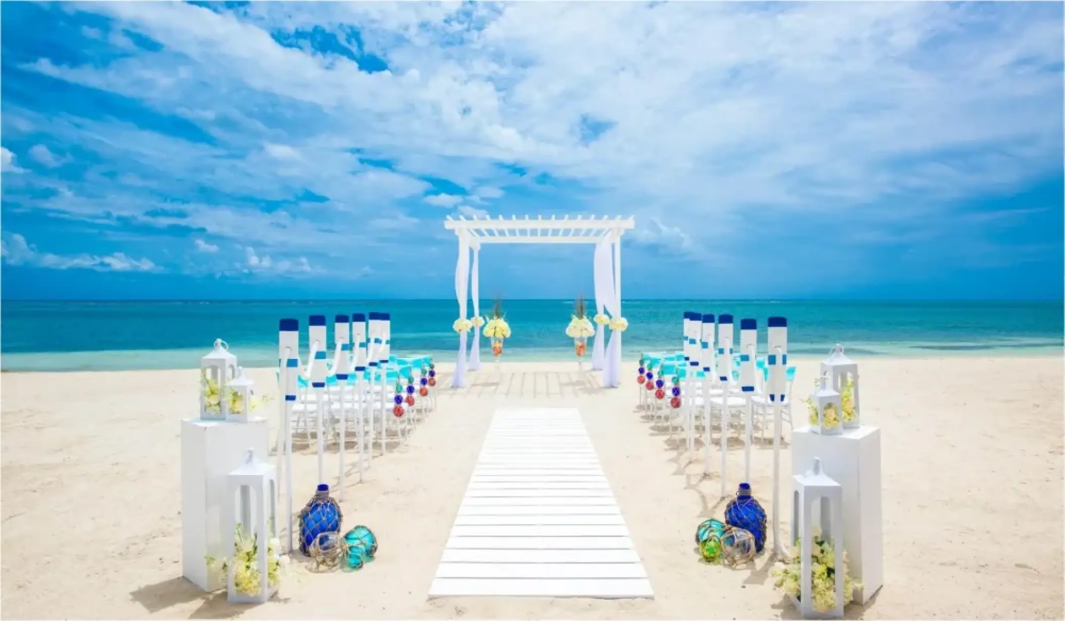 Beachfront wedding ceremony with white pergola and blue accents at Sandals Montego Bay, Montego Bay