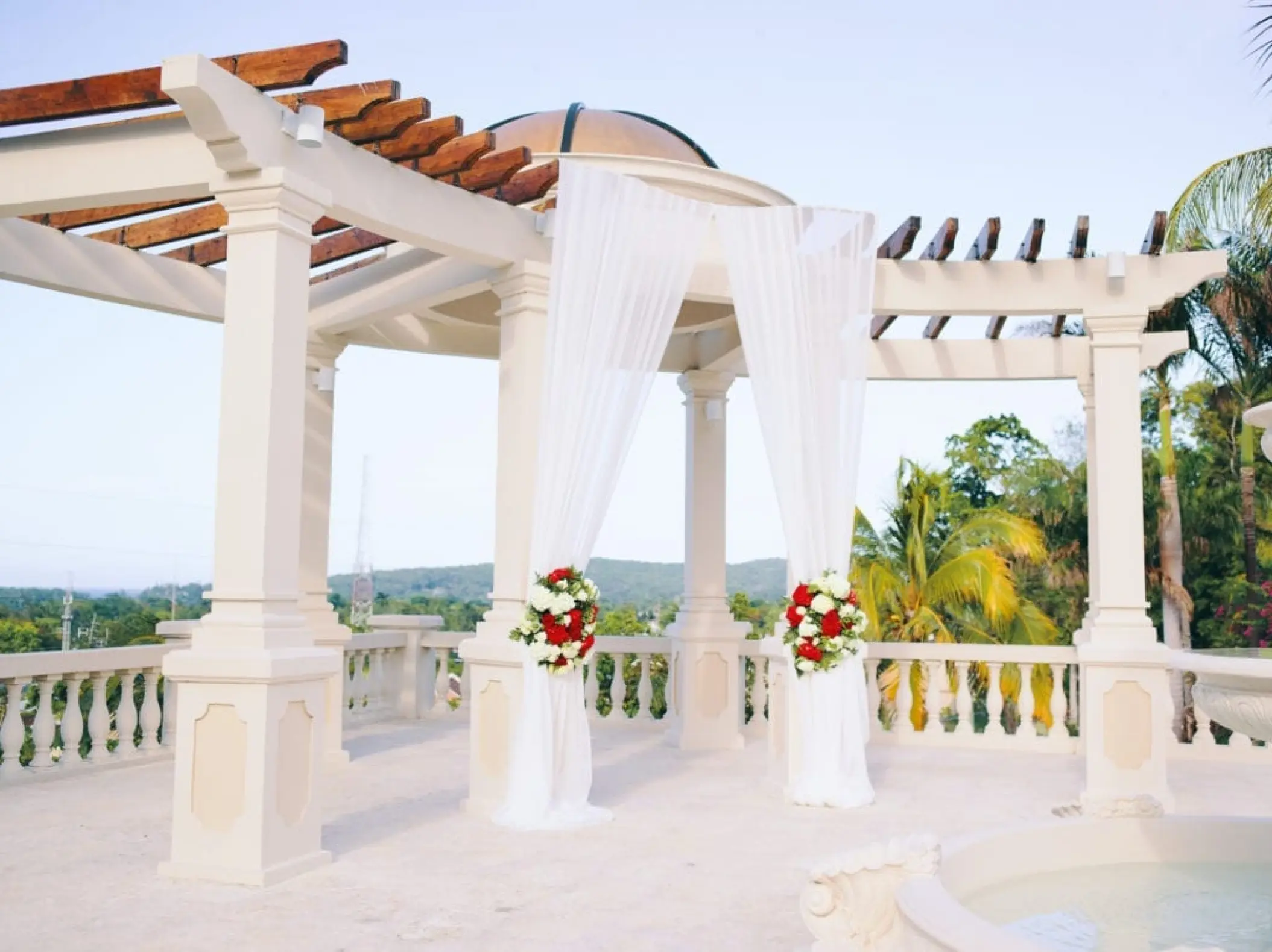 White wedding gazebo with draped fabric and red floral arrangements at Sandals Ochi, Ocho Rios