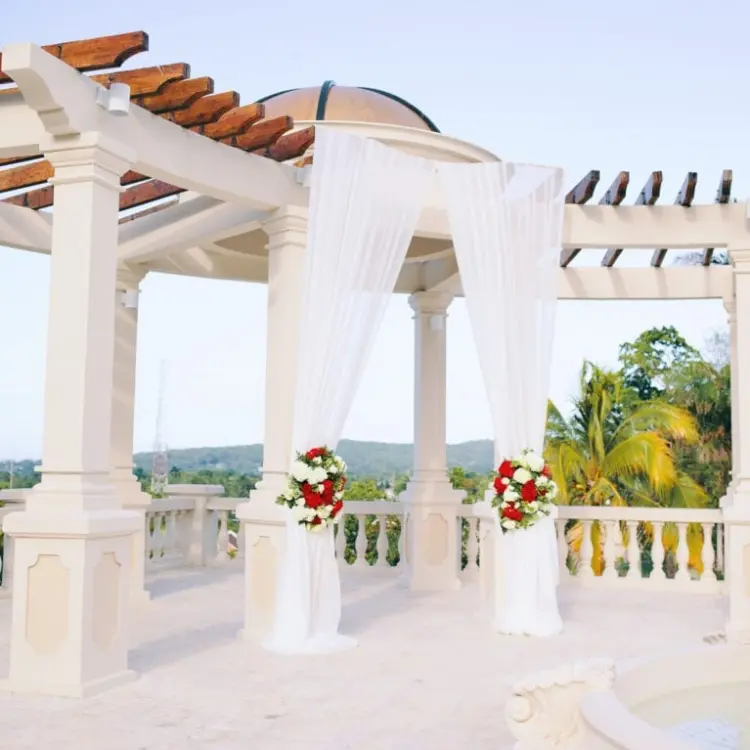 White wedding gazebo with draped fabric and red floral arrangements at Sandals Ochi, Ocho Rios