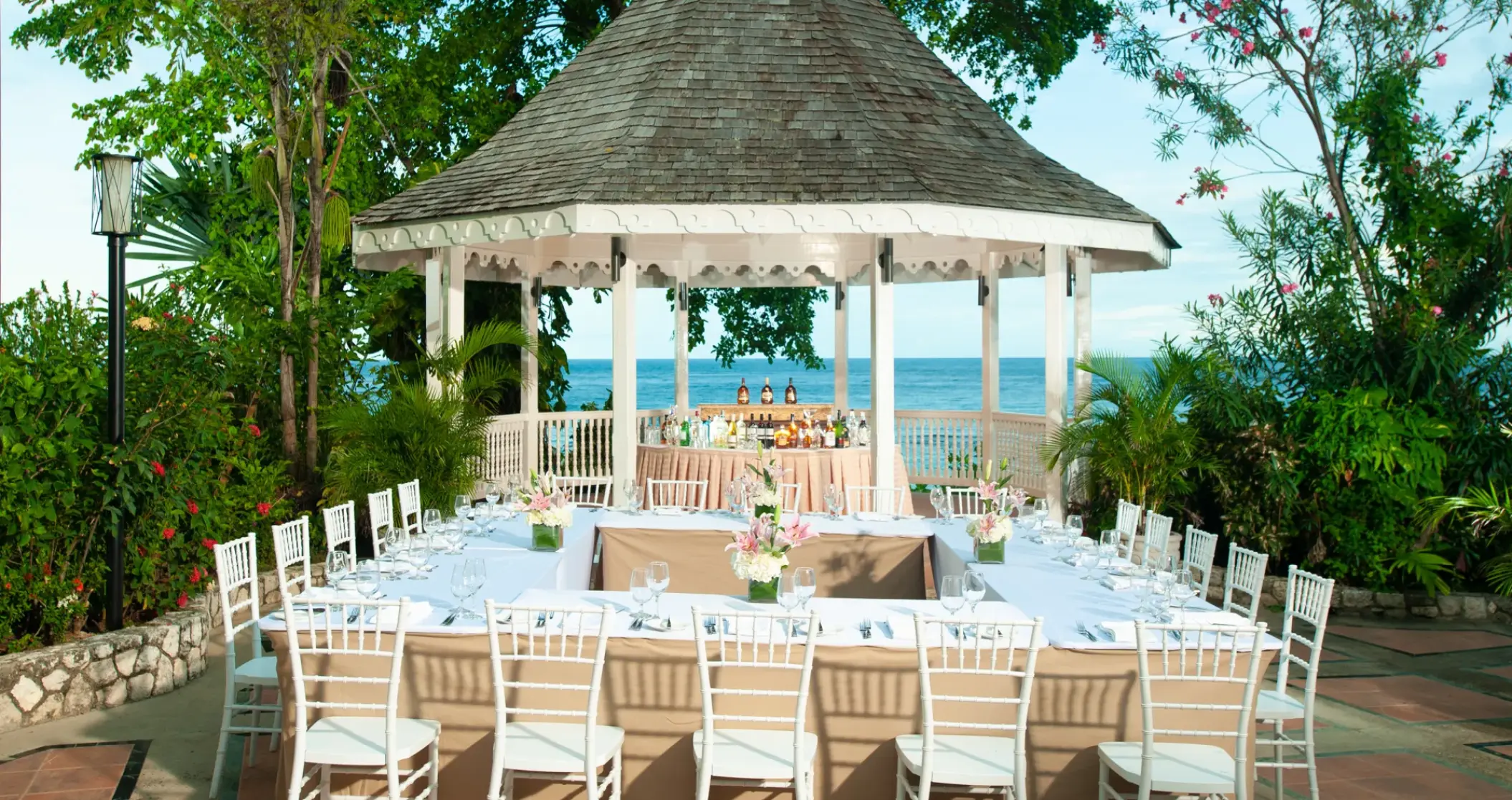 Outdoor wedding reception with white chairs and floral decor at a garden gazebo in Sandals Ochi, Ocho Rios