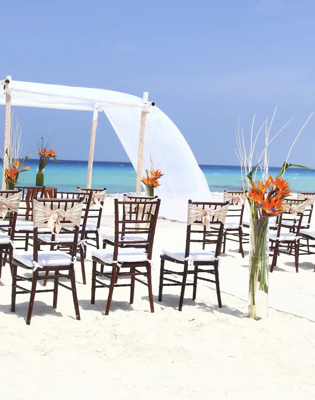 Beachfront wedding ceremony with white draped huppah and wooden chairs at Sandos Cancun, Cancun