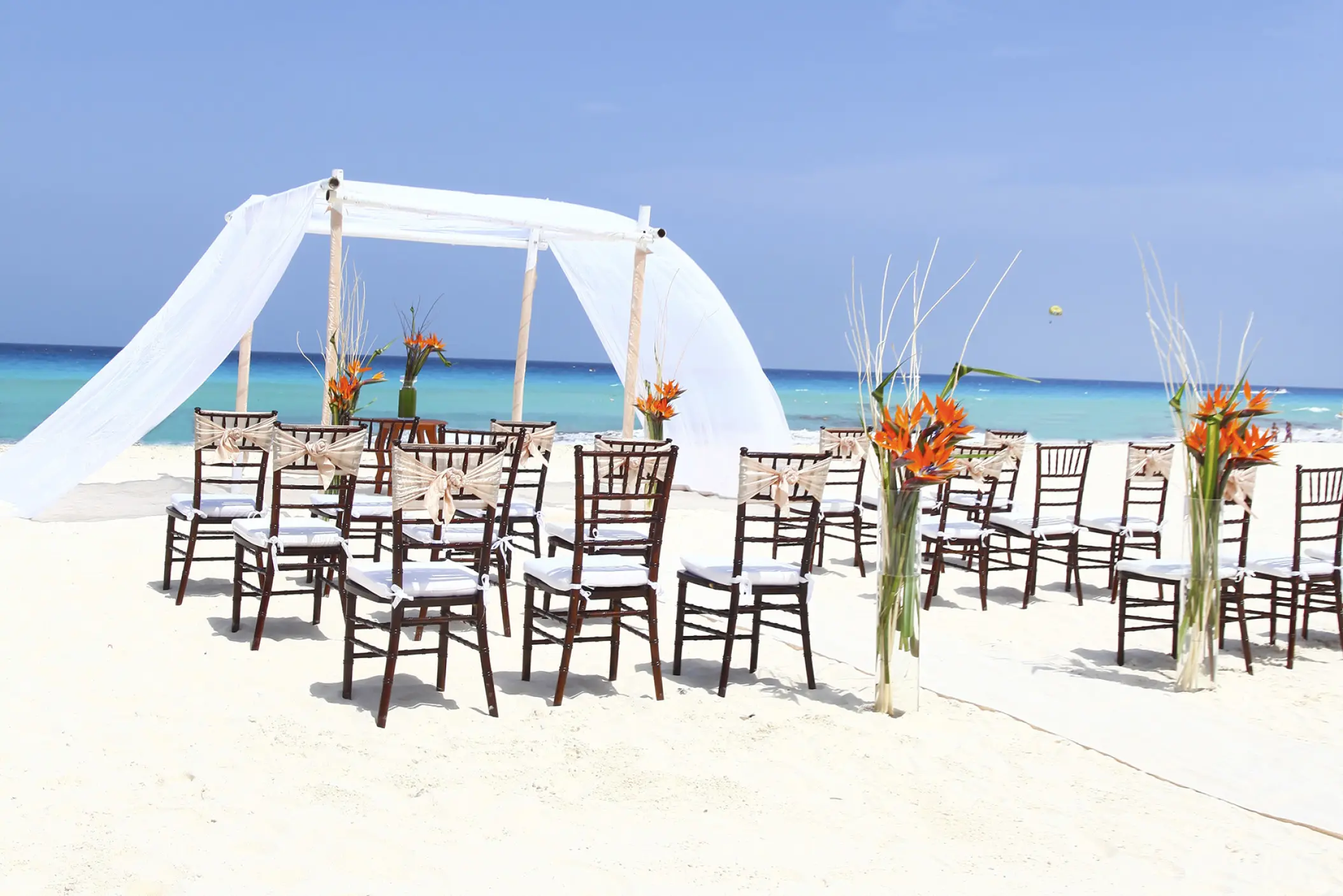 Beachfront wedding ceremony with white draped huppah and wooden chairs at Sandos Cancun, Cancun