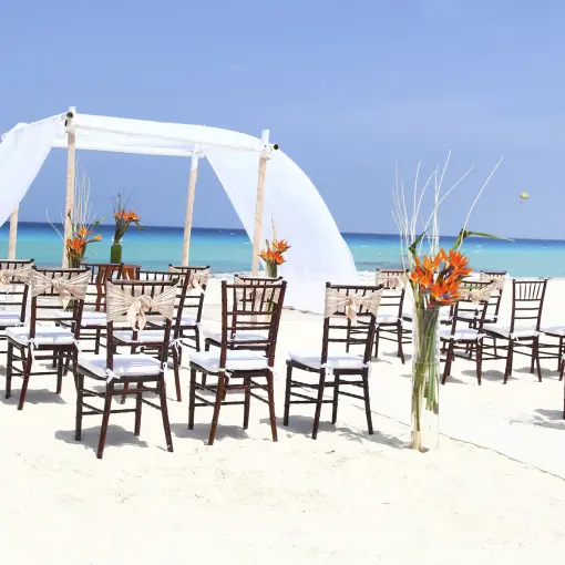 Beachfront wedding ceremony with white draped huppah and wooden chairs at Sandos Cancun, Cancun