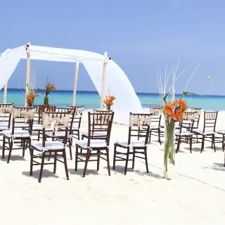 Beachfront wedding ceremony with white draped huppah and wooden chairs at Sandos Cancun, Cancun