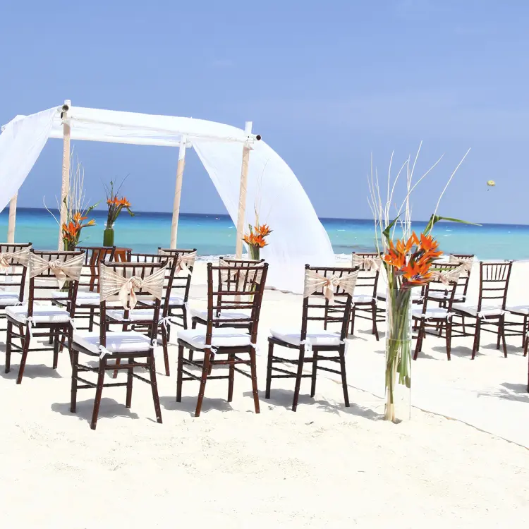 Beachfront wedding ceremony with white draped huppah and wooden chairs at Sandos Cancun, Cancun