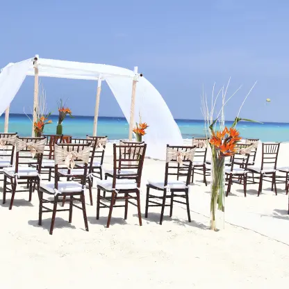 Beachfront wedding ceremony with white draped huppah and wooden chairs at Sandos Cancun, Cancun